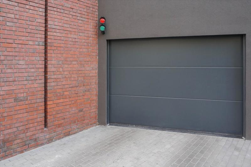Porte de garage grise à finition lisse le long d'un mur en brique